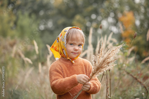 Autumn portrait of beautiful little smiling girl in a yellow shawl in the tall grass. photo