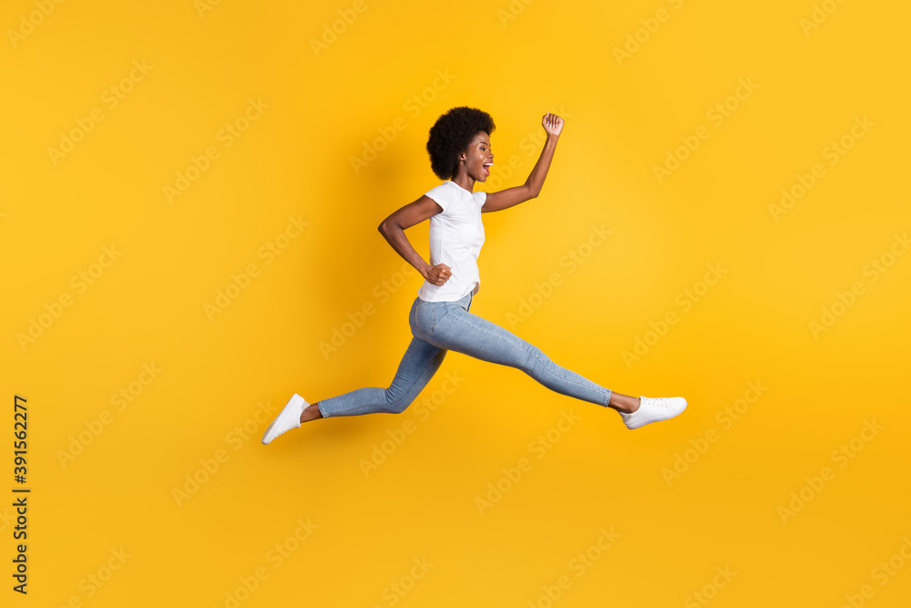 Full length body size photo of young female millennial with black skin jumping high running fast cheering isolated on bright yellow color background