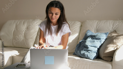 Young woman wears headset conference calling on laptop talks with online teacher studying, working from home. Lady student learning using computer webcam chat makes notes. Distance education concept