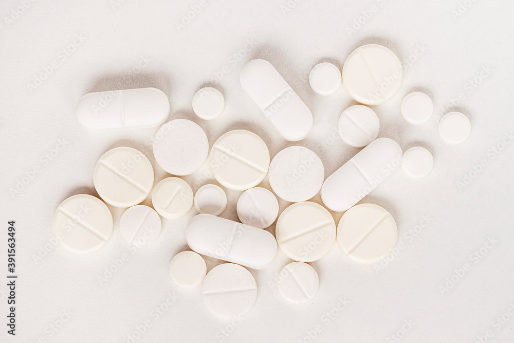 White tablets and capsules of different sizes lie on an light surface, close-up, top view. Medicines and treatment concept. White tablets and capsules of different sizes lie on an light surface, close-up, top view. Medicines and treatment concept.
