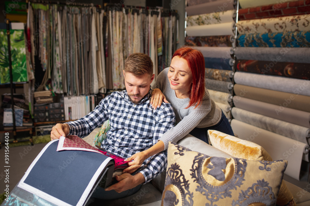 Assortment. Couple choosing textile at home decoration store, shop. Making of home interior design during quarantine. Happy man and woman, young family look dreamful, cheerful choosing materials.