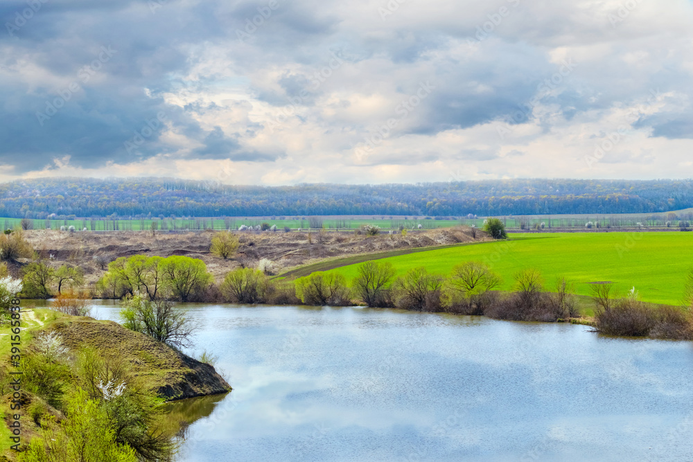 Spring landscape with river, green field and picturesque cloudy sky