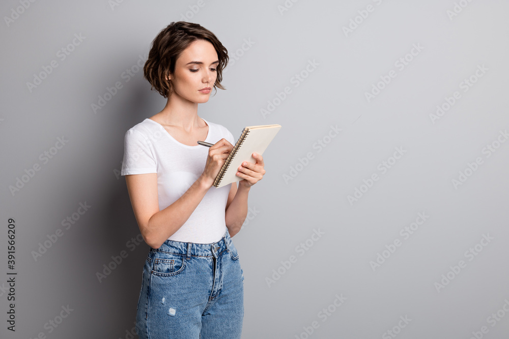 Photo of young attractive woman serious thoughtful write plan to-do list notebook isolated over grey color background Photo of young attractive woman serious thoughtful write plan to-do list notebook isolated over grey color background