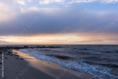 Rock groyne with waves and scenic evening sky by Baltic Sea shore at dawn.