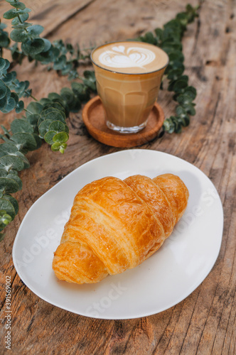 Croissant in white plate and hot milk coffee latte on a wooden table