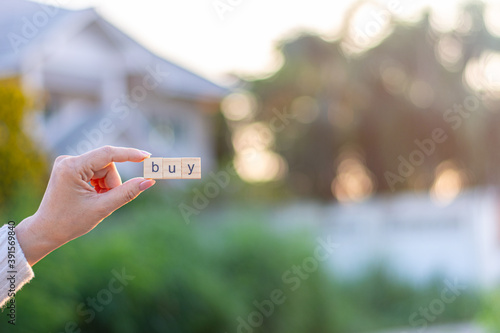 "BUY" alphabet in woman hand front a home. - buy house and real estate concept.