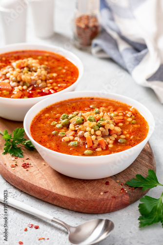 Vegetarian soup with vegetables, green peas, couscous (ptitim paste) and lentils in a white bowl close-up. Maghreb soup berkoukes. North African cuisine.