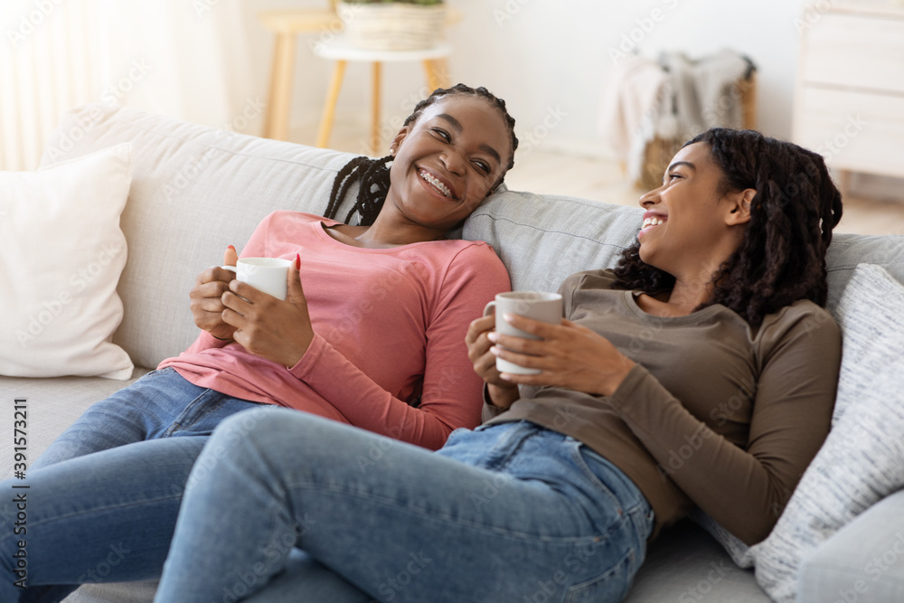 Relaxed black ladies drinking tea, talking while resting on couch Relaxed black ladies drinking tea, talking while resting on couch
