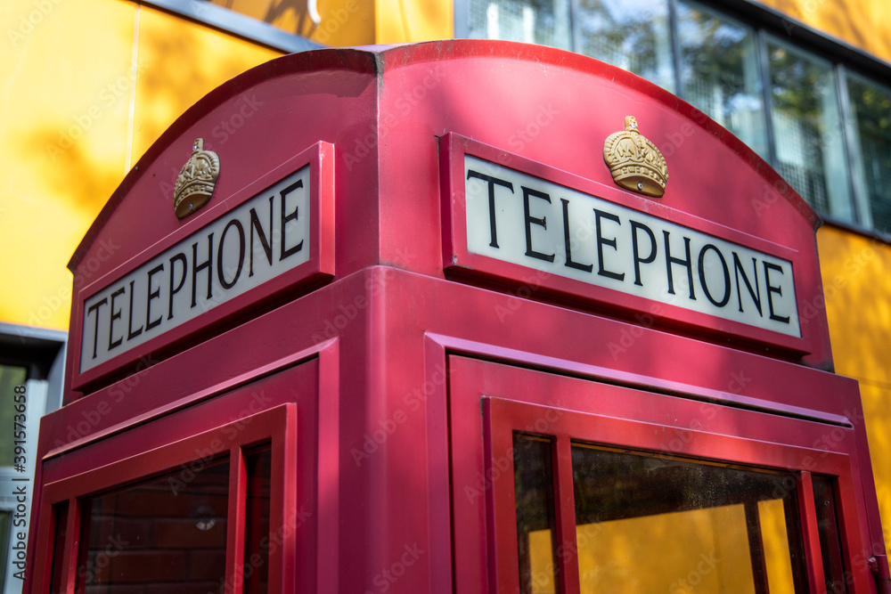 Traditional Red British Telephone Box Against A yellow Wall Traditional Red British Telephone Box Against A yellow Wall