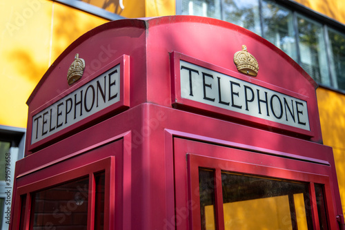 Traditional Red British Telephone Box Against A yellow Wall