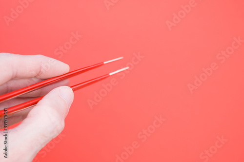 Wall Mural Hand holding a red hair tweezer on red background with a copy space