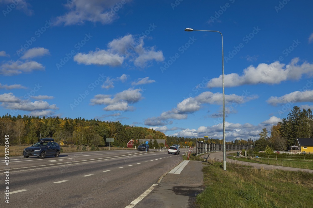 Beautiful autumn landscape view. Asphalt road on yellowed trees and blue sky white white clouds background. 