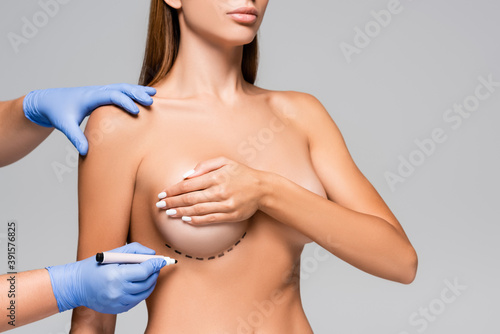 Cropped view of doctor holding marker near bust of naked woman with marks isolated on grey