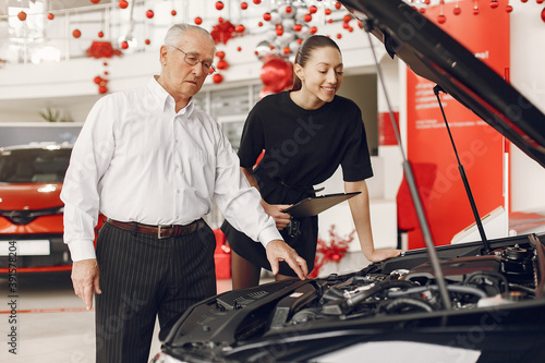 Senior in a car salon. Old man buying the car. Elegant woman helps a man buy a car.
