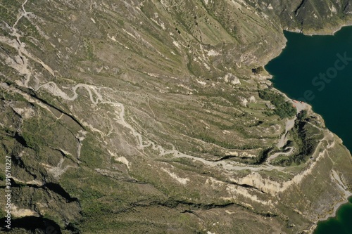Aerial view of a small restaurant next to the large, blue lake in the vulcanic crater of Quilotoa at the bottom of the steep hills