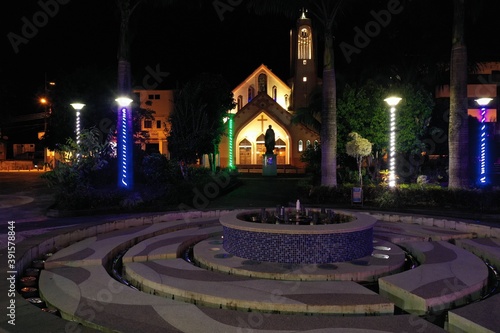 Puyo, Ecuador, 19-6-2020: night view a fontain in a public park with a church in the background © pangamedia
