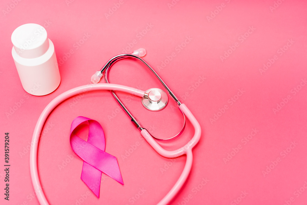 Stethoscope near pink ribbon of breast cancer awareness and jar with pills on pink background