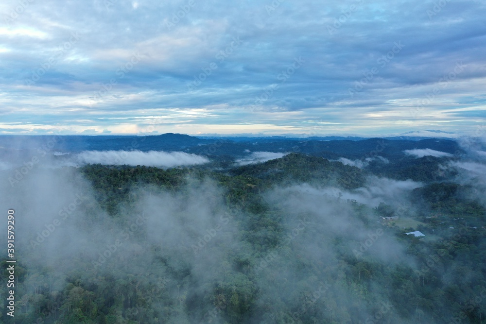 Aerial view of a tropical rainforest covered in fog with a small indigenous community visible through the fog