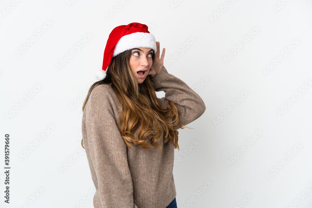 Caucasian girl with christmas hat isolated on white background listening to something by putting hand on the ear