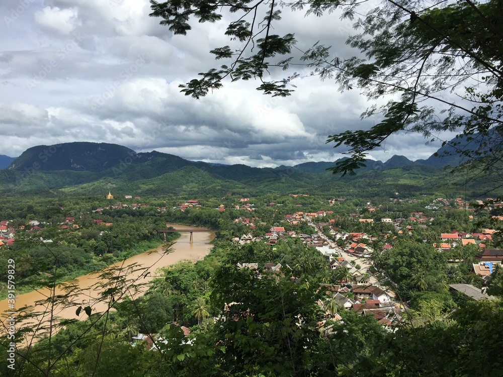 Tropical city in Laos, South East Asia that is divided by a large brown colored river seen from a distance