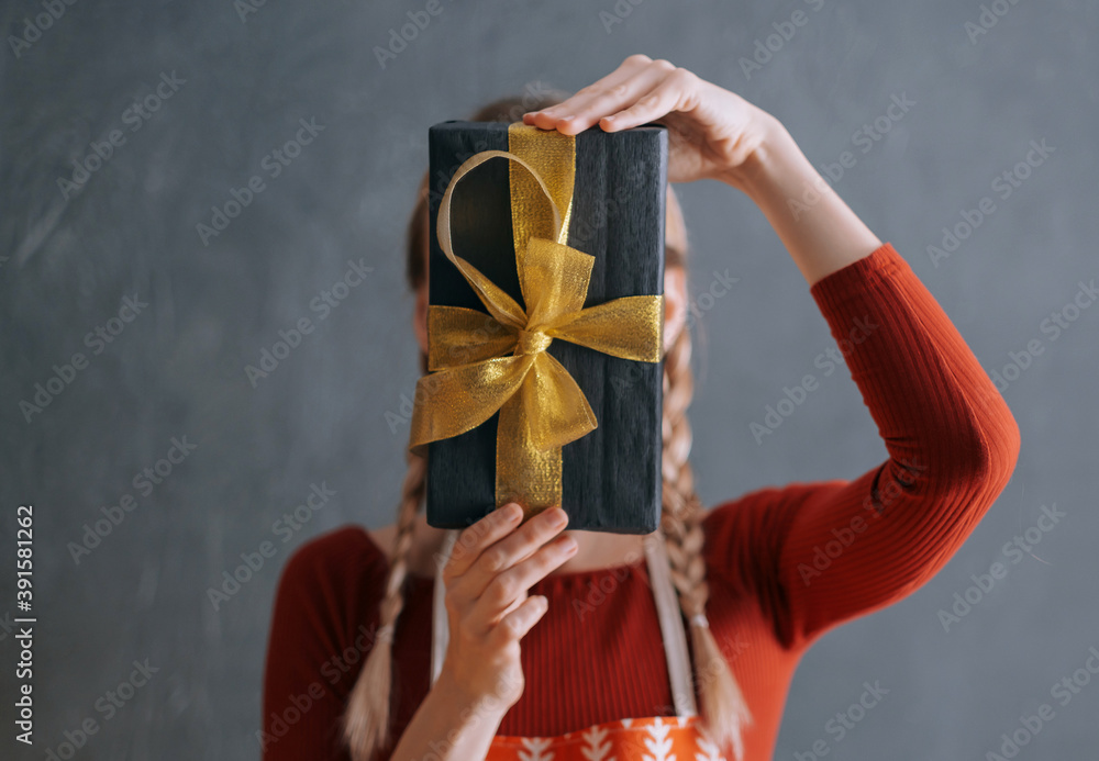 woman holding a box with a christmas present in her hands in front of her face woman holding a box with a christmas present in her hands in front of her face