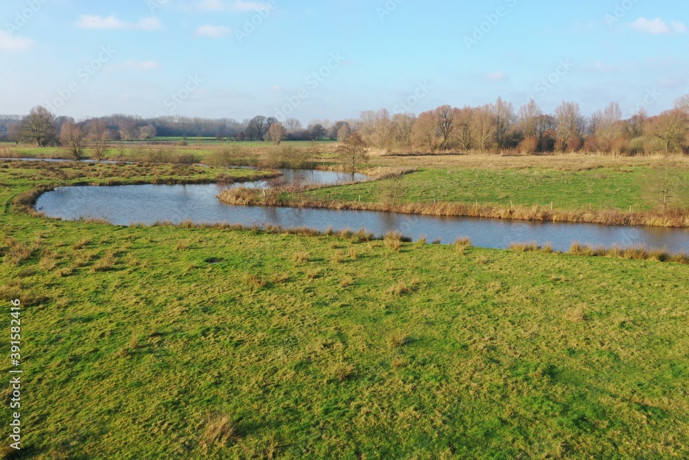 view over a small river that is meandering through the meadows and bare trees in winter
