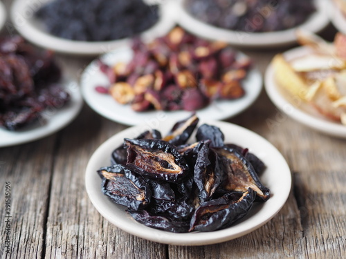 Dried plum on the foreground. Background with bowls with various dried fruits on a wooden ancient background. Home preparation of dried fruits.