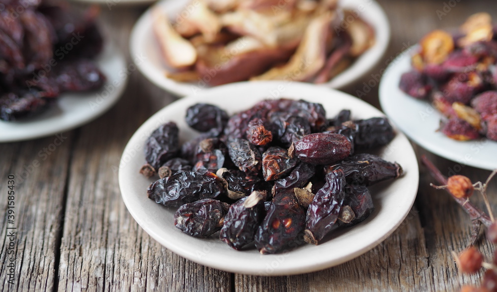 Dried rose hips on the foreground. Background with bowls with various dried fruits on a wooden ancient background.Home preparation of dried fruits. Dried rose hips on the foreground. Background with bowls with various dried fruits on a wooden ancient background.Home preparation of dried fruits.