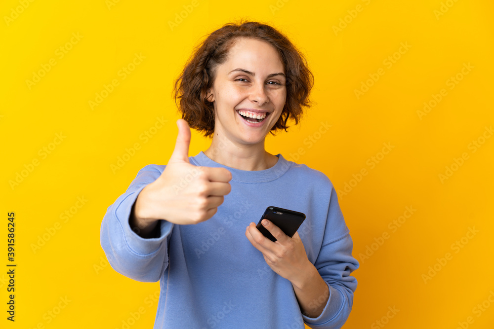 Young English woman isolated on pink background using mobile phone while doing thumbs up Young English woman isolated on pink background using mobile phone while doing thumbs up