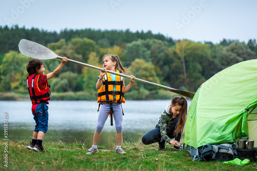 Little funny children arguing about paddle near tent in camping site close to river