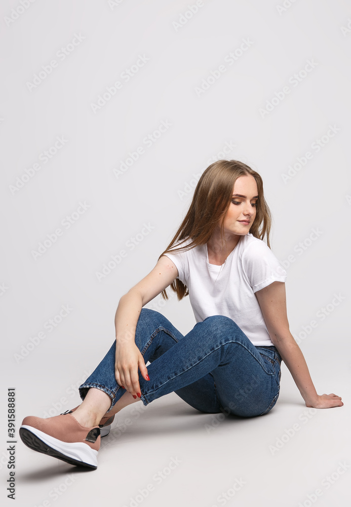 young beautiful woman in a white t-shirt and jeans on a white background. Young woman sit on white background. Photo concept for advertisements of clothes and shoes young beautiful woman in a white t-shirt and jeans on a white background. Young woman sit on white background. Photo concept for advertisements of clothes and shoes
