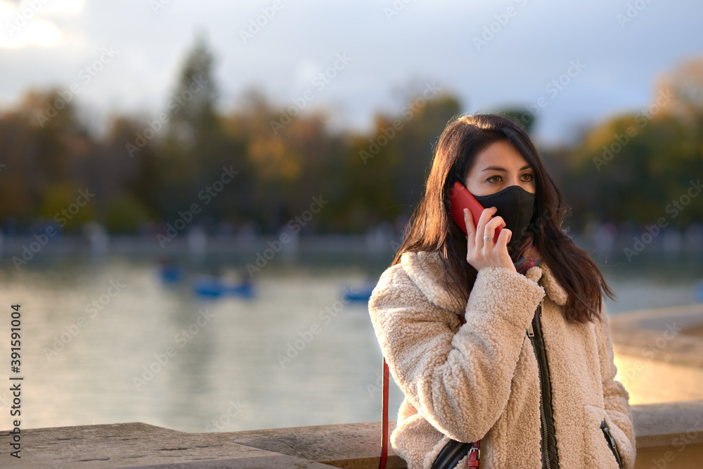 Beautiful woman with facemask calling with her smartphone in a park in autumn