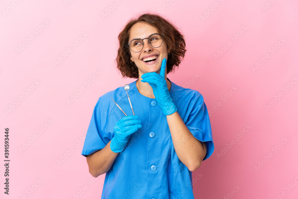 Woman English dentist holding tools over isolated on pink background thinking an idea while looking up Woman English dentist holding tools over isolated on pink background thinking an idea while looking up