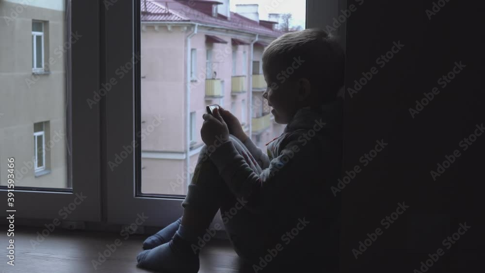 Sad lonely boy with smartphone on windowsill. View of autumn Park and street space for text. Danger of internet Sad lonely boy with smartphone on windowsill. View of autumn Park and street space for text. Danger of internet