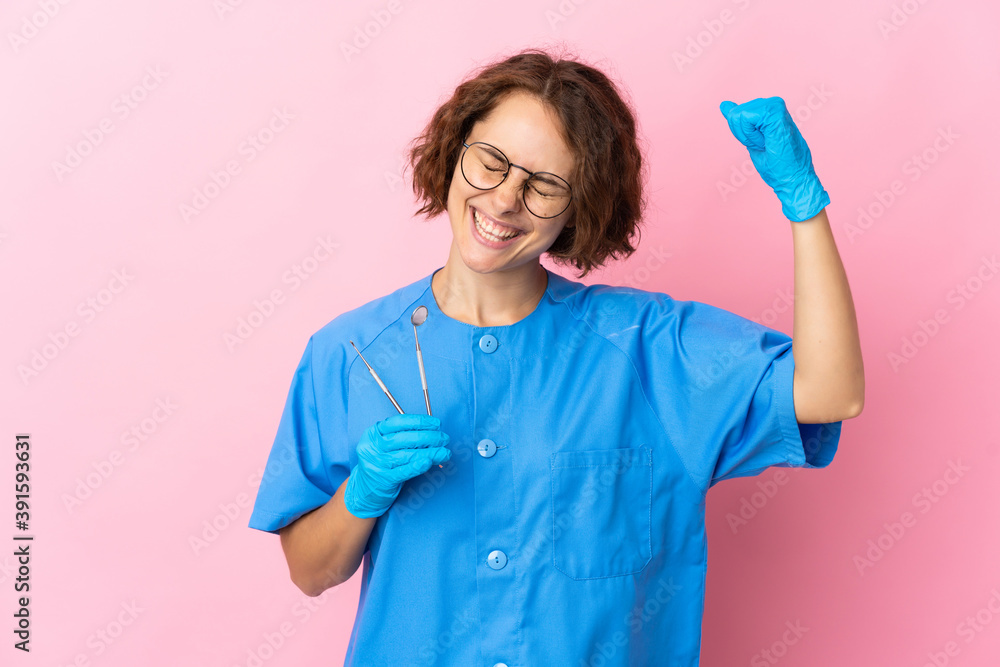 Woman English dentist holding tools over isolated on pink background celebrating a victory Woman English dentist holding tools over isolated on pink background celebrating a victory
