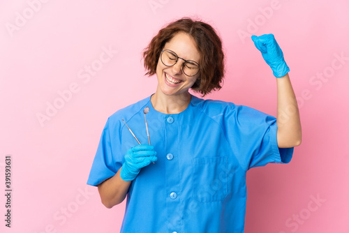 Woman English dentist holding tools over isolated on pink background celebrating a victory