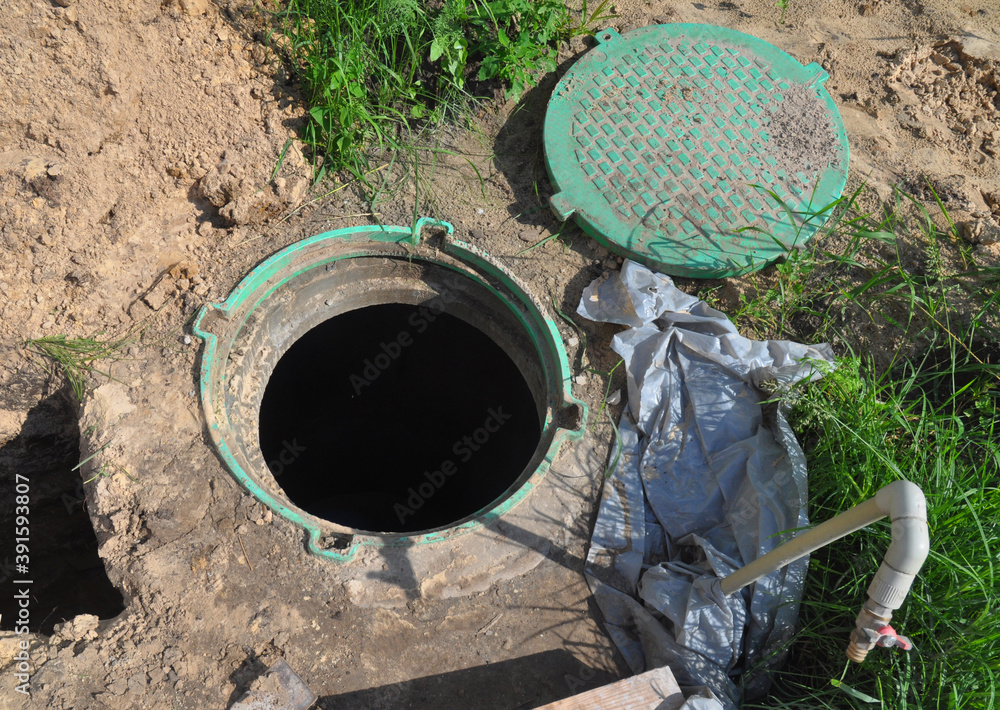 A close-up of a borehole pump house, station and water supply system with a manhole cover lid open to provide maintenance service. A close-up of a borehole pump house, station and water supply system with a manhole cover lid open to provide maintenance service.