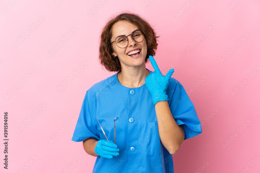 Woman English dentist holding tools over isolated on pink background giving a thumbs up gesture