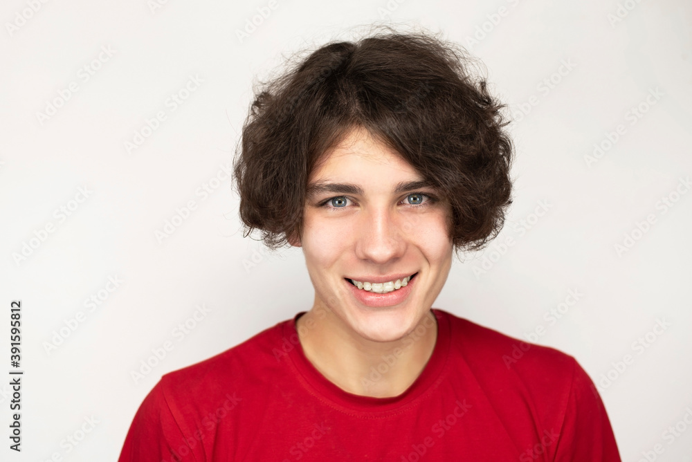 Cute teenager guy sincerely smiles on a light background, he has plastic dental braces on his teeth to align teeth correction Cute teenager guy sincerely smiles on a light background, he has plastic dental braces on his teeth to align teeth correction