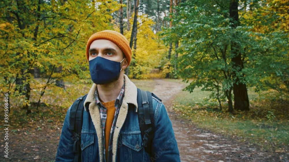 Young tourist man walking in forest, wearing medical protective mask, safe travel, hiking in park, slow motion Young tourist man walking in forest, wearing medical protective mask, safe travel, hiking in park, slow motion