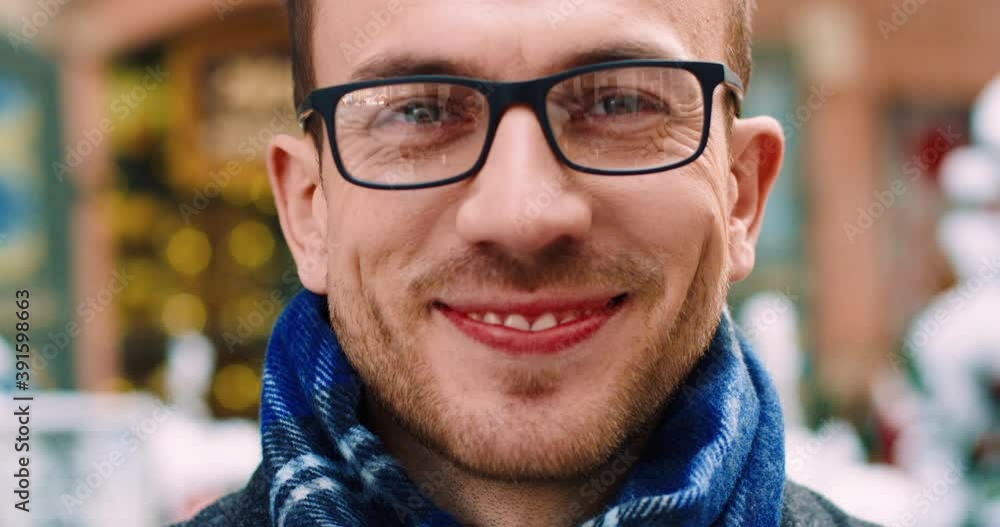 Close-up portrait of handsome caucasian man in coat and glasses standing on snowy street and smiling at camera. Close-up portrait of handsome caucasian man in coat and glasses standing on snowy street and smiling at camera.
