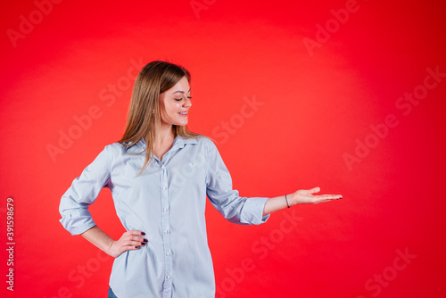 Young woman showing product on empty copy space on open hand palm. Beautiful model isolated on red background