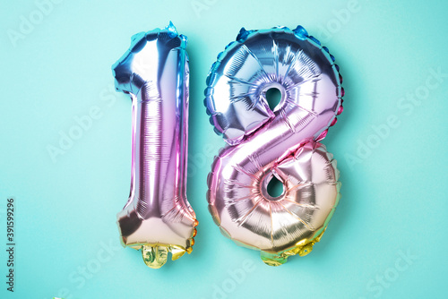 Fototapeta Naklejka Na Ścianę i Meble -  Creative layout. Rainbow foil balloon number, digit eighteen. Birthday greeting card with inscription 18. Anniversary concept. Top view. Stylish colored numeral on blue background. Numerical digit