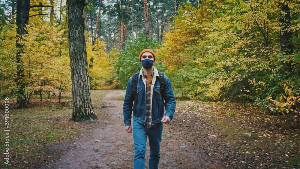 Slow motion shot of young male tourist in protective mask walking alone in autumn forest Slow motion shot of young male tourist in protective mask walking alone in autumn forest