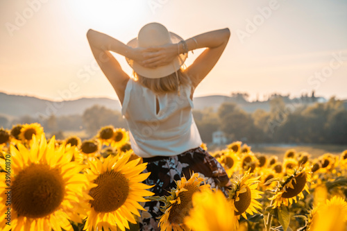 Ragazza felice con cappello di paglia guarda il tramonto in un campo di girasole photo