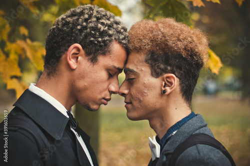 Handsome young gay couple standing head to head in park during autumn. Concept of same sex love, equality and LGBT rights. Black lives matter! photo