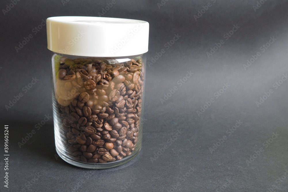 transparent glass jar with a white plastic lid filled with roasted coffee beans on a dark background side view transparent glass jar with a white plastic lid filled with roasted coffee beans on a dark background side view