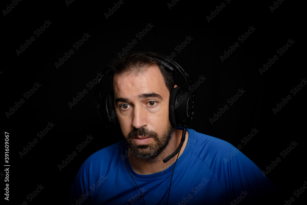 Bearded man dressed in blue t-shirt and with headphones posing on black background