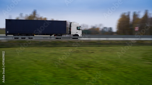 Biała ciężarówka z niebieskim kontenerem na autostradzie. Rozmyte tło