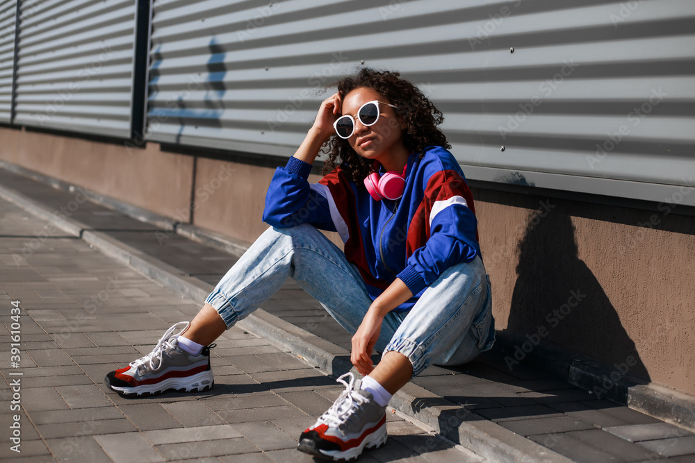Cool black girl with curly hair, glasses, 90s, 80s, retro hip hop style,  dancing against a metal wall, dynamics and expression Stock Photo